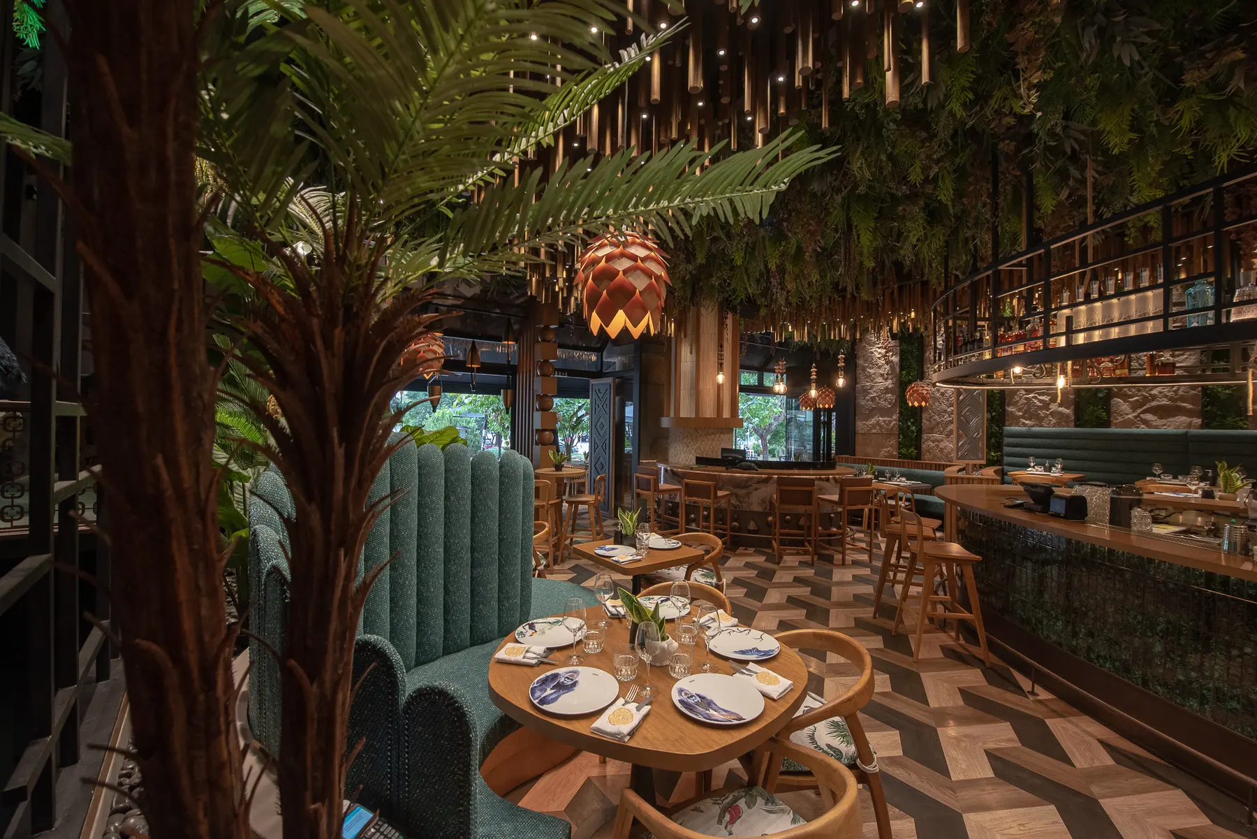 La sala di Iguazu Athens: una palma in primo piano, bambù appeso al soffitto e divanetti di velluto verde